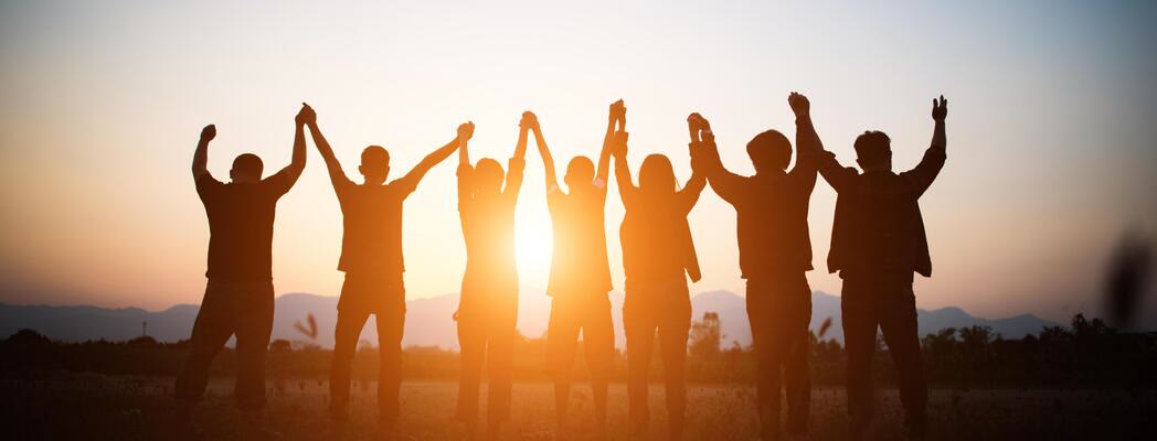 A joyful team celebrating together with raised hands at sunset